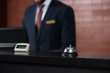Recepcjonista w hotelu, dzwonek i komputer. Zastanawiasz się, ile zarabia recepcjonistka w hotelu?